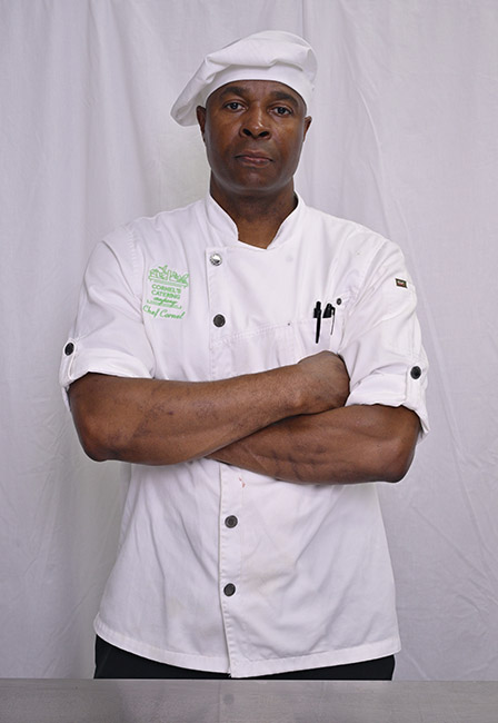 Chef Cornel Robinson standing confidently with arms crossed, wearing a white chef’s coat and toque embroidered with the Cornel’s Catering Co. logo. Posing against a plain white backdrop.