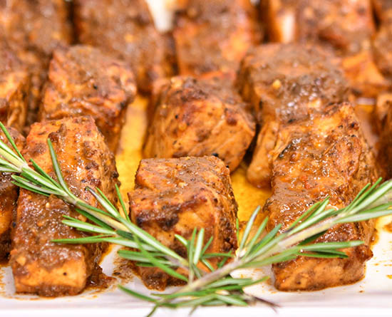 Tray of marinated chicken bites coated in brown sauce, garnished with rosemary sprigs