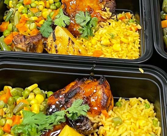 Meal prep containers filled with yellow rice, mixed vegetables, and roasted chicken drumsticks