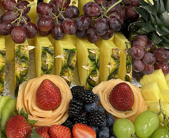 Colorful fruit platter with sliced pineapple, red grapes, strawberries, blackberries, and cantaloupe roses