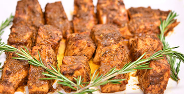 Tray of marinated chicken bites coated in brown sauce, garnished with rosemary sprigs
