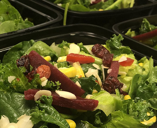 Close-up of fresh salad with kale, beets, corn, and sliced almonds in black container