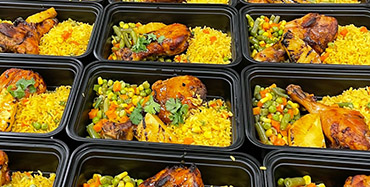Meal prep containers filled with yellow rice, mixed vegetables, and roasted chicken drumsticks