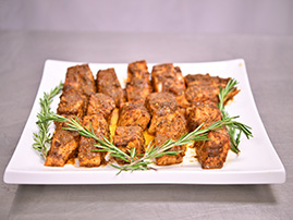 Tray of marinated chicken bites coated in brown sauce, garnished with rosemary sprigs