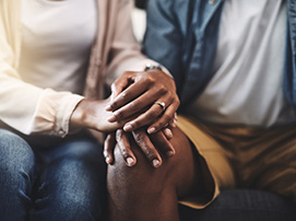 Close-up of two people sitting together, holding hands in a comforting gesture.