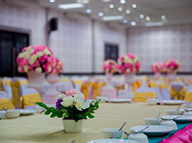 Elegant banquet hall with round tables, floral centerpieces, and chairs decorated in gold and pink covers.
