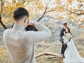 Photographer capturing an outdoor wedding portrait of a bride and groom in a park with autumn leaves